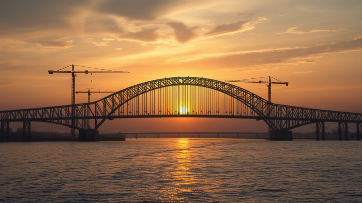 A modern arch bridge crossing a wide river at dusk, with construction cranes alongside